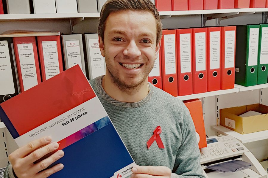 Deniz Kurku mit Broschüre der Aids-Hilfe